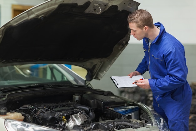 Meccanico con appunti esaminando il motore dell&#39;auto