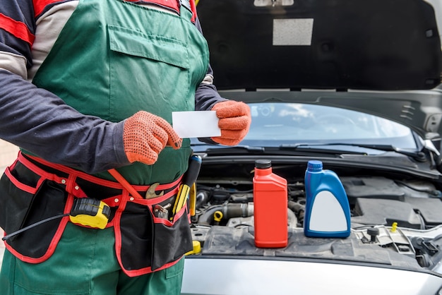 Meccanico con biglietto da visita in posa vicino all'auto con il cofano aperto