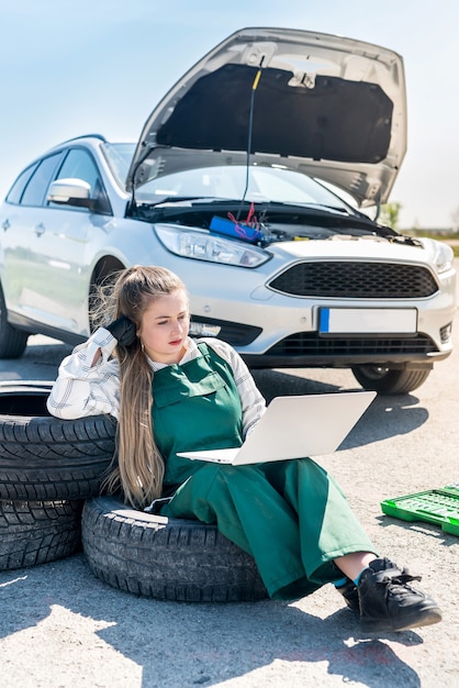 Meccanico con laptop che diagnostica un'auto rotta sul ciglio della strada