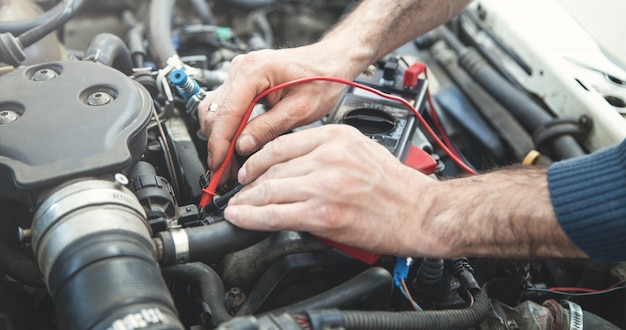 Meccanico con un multimetro che prova il motore dell'auto. Servizio auto