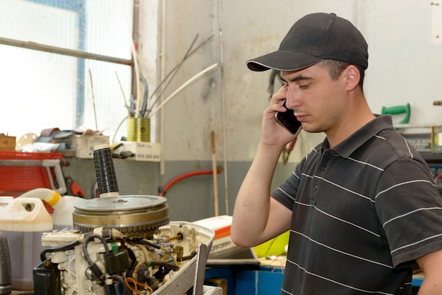 Meccanico del giovane che ripara le imbarcazioni a motore e il telefono al cliente