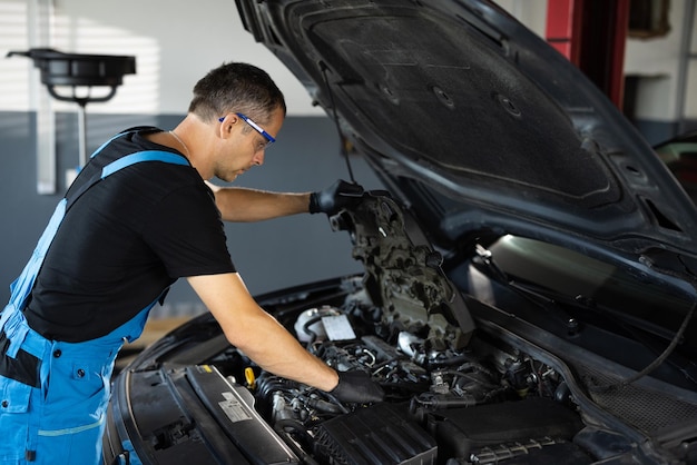 Meccanico di auto che nota le parti di riparazione durante la riparazione del motore del cofano dell'auto aperto presso il meccanico di officina