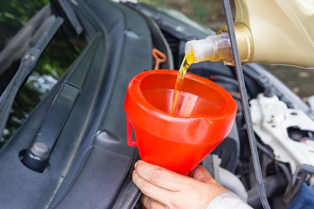 Meccanico di automobile che sostituisce e versando l&#39;olio fresco nel motore al servizio di riparazione di manutenzione