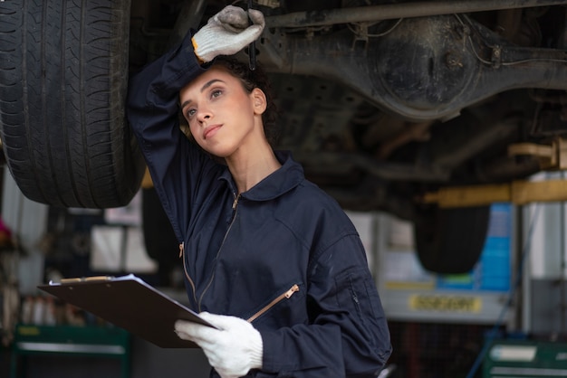 Meccanico femminile stressato che lavora sodo per riparare un'auto nel garage di servizio auto