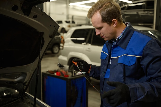 Meccanico in garage che controlla il livello dell'olio motore in un'auto. Tecnico automobilistico in officina. Manutenzione dell'automobile e concetto di servizio automatico