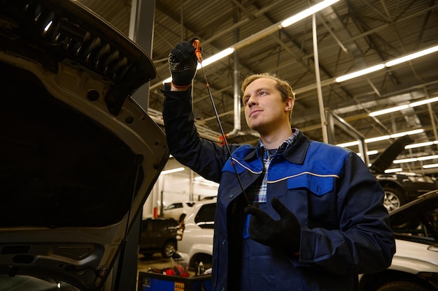 Meccanico in garage che esamina l'astina di livello dell'olio motore dell'auto controllando il livello dell'olio motore in un'auto. Tecnico automobilistico in officina. Manutenzione dell'automobile e concetto di servizio automatico