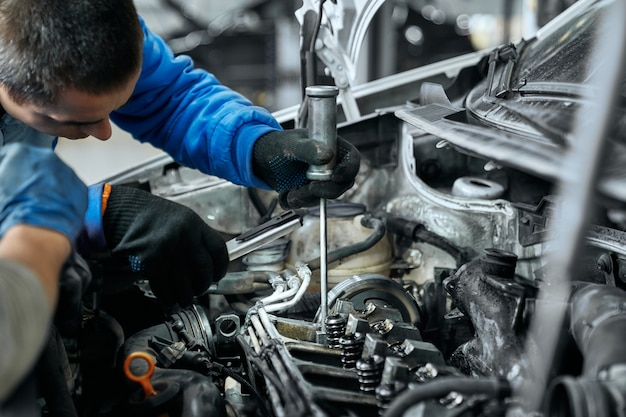 Meccanico in uniforme blu che sostituisce le candelette nel motore