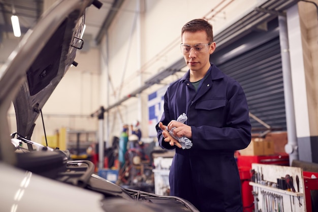 Meccanico maschio del motore che pulisce le mani dopo aver lavorato sul motore dell'auto in garage