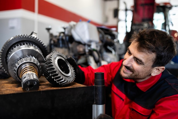 Meccanico o serviceman esperto che tiene le parti degli ingranaggi all'interno dell'officina