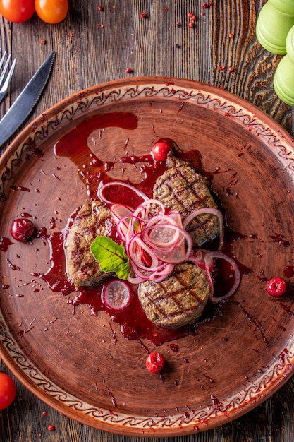 Medaglioni di vitello con salsa di ciliegie, serviti con cipolle e ravanelli sott'aceto, un piatto gourmet, orientamento verticale, vista dall'alto