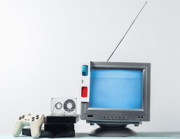 Media retrò, intrattenimento anni '80. Antenna ricevitore tv retrò vecchio stile, occhiali stereo anaglifi, audio e videocassetta, gamepad sul muro bianco.