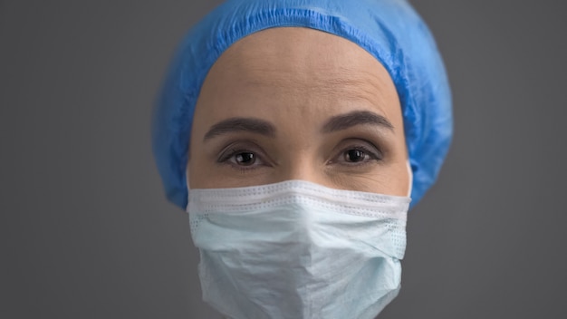 Medic femminile in maschera protettiva e cappuccio blu, chiudere il viso isolato su grigio indietro