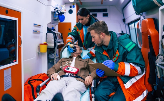 Medici di emergenza o paramedici stanno lavorando con un paziente anziano mentre giace su una barella in un'ambulanza.