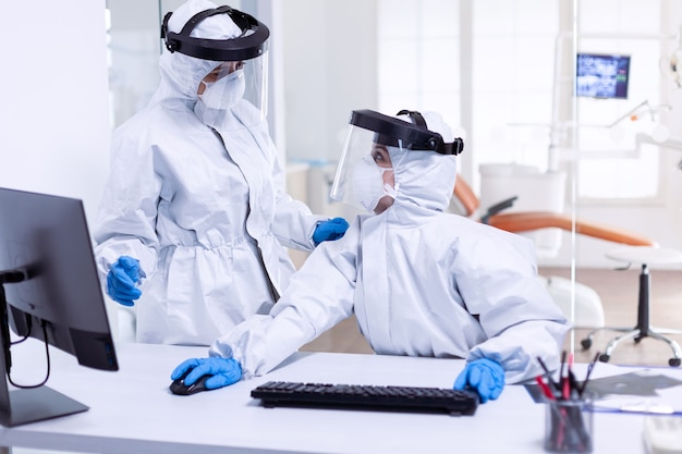 Medici donne in tuta protettiva per combattere la pandemia con covid-19 nella reception dentale. Squadra di medicina che indossa indumenti di protezione contro la pandemia di coronavirus nella ricezione dentale come precauzione di sicurezza.