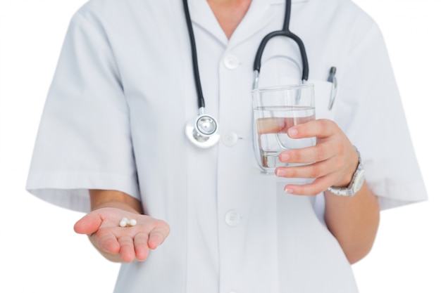 Medicina e bicchiere d&#39;acqua della tenuta dell&#39;infermiere su fondo bianco