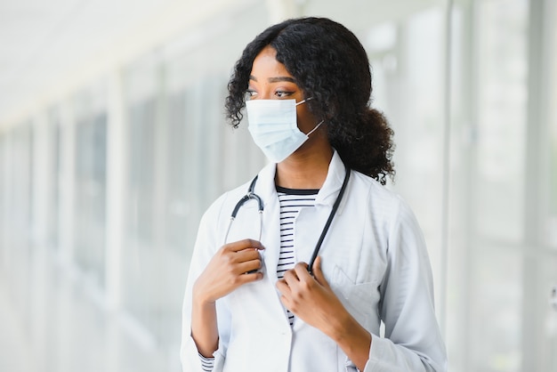 Medico africano americano femminile, infermiera donna che indossa cappotto medico con stetoscopio e maschera. Felice eccitato per il successo operaio medico in posa su sfondo chiaro. Concetto di pandemia, covid 19