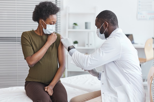 Medico africano in camice bianco che vaccina una donna incinta durante la sua visita in ospedale