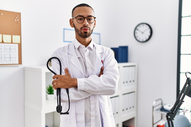 Medico afroamericano che tiene lo stetoscopio in clinica guardando la telecamera che soffia un bacio essendo adorabile e sexy. espressione d'amore.