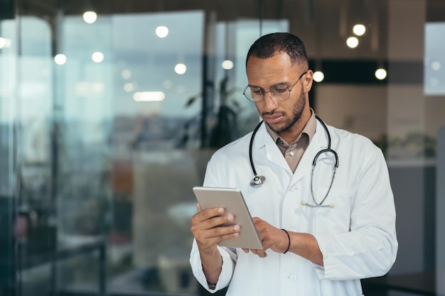 Medico afroamericano serio e concentrato che utilizza computer tablet uomo che lavora all'interno moderno