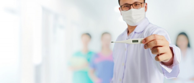 Medico asiatico che indossa una maschera protettiva e che mostra un termometro
