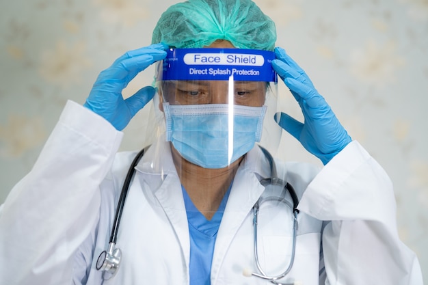 Medico asiatico che indossa uno schermo facciale e una tuta DPI per proteggere il Coronavirus Covid-19.