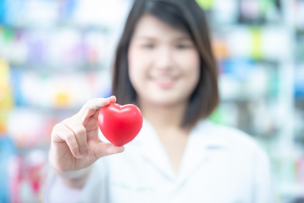 Medico asiatico delle donne che tiene una palla rossa del cuore con il concetto vago della sanità.