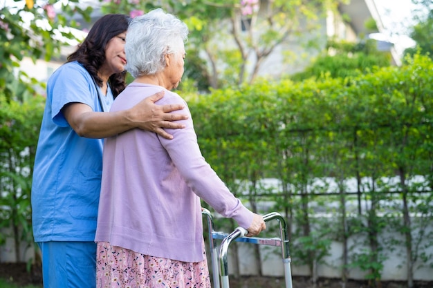 Medico caregiver aiuto e cura Paziente donna anziana asiatica cammina con camminatore nel parco dell'ospedale