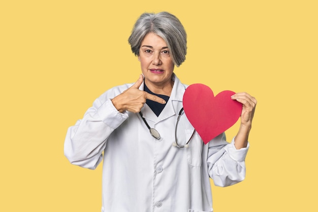 Medico caucasico di mezza età con il simbolo del cuore persona che indica con la mano una camicia copia spazio orgoglioso e sicuro