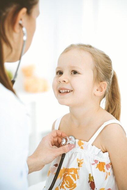 Medico che esamina una bambina con lo stetoscopio. Paziente bambino sorridente felice alla normale ispezione medica. Concetti di medicina e assistenza sanitaria.