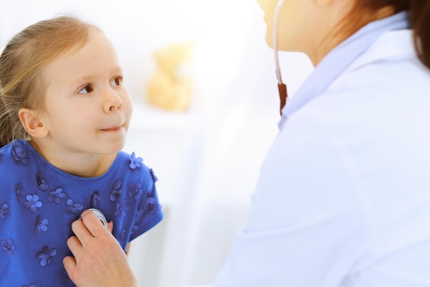 Medico che esamina una bambina con lo stetoscopio. Paziente bambino sorridente felice alla normale ispezione medica. Concetti di medicina e assistenza sanitaria.