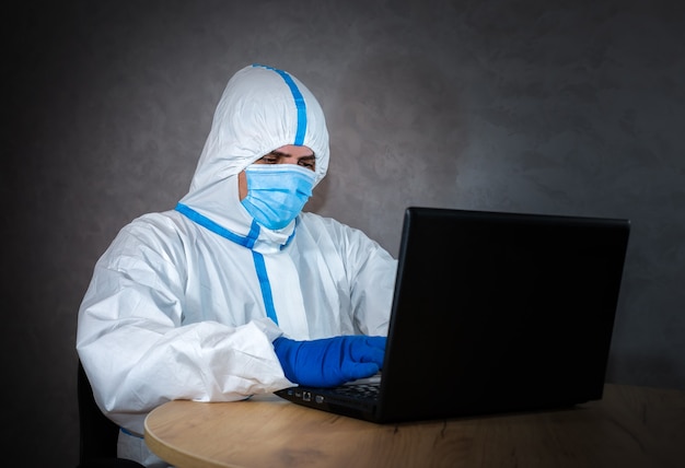 Medico che indossa tuta protettiva medica, maschera medica e guanti che lavorano sul laptop. Protezione dall'epidemia di virus. Coronavirus (COVID-19). concetto di assistenza sanitaria. Lavoro a distanza in una pandemia covid.