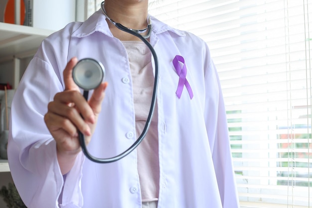 medico che indossa un nastro viola sull'uniforme e mostra lo stetoscopio Giornata mondiale del cancro