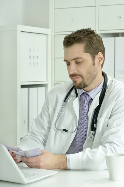 Medico che lavora con laptop e soldi in ufficio