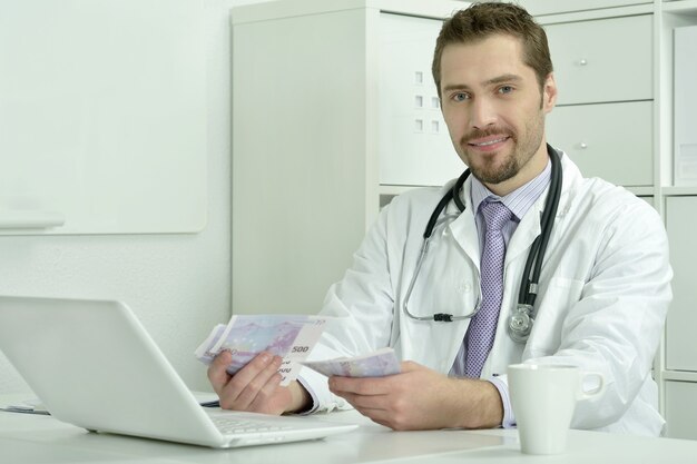 Medico che lavora con laptop e soldi in ufficio