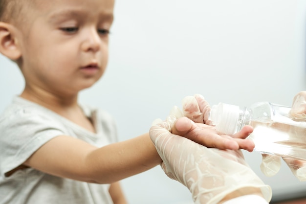 Medico che mette disinfettante per le mani sulle mani del bambino