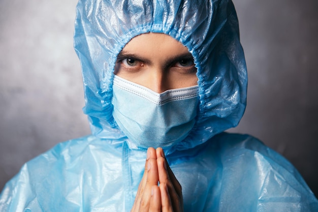 Medico che prega per i pazienti che indossano tuta protettiva e maschera facciale