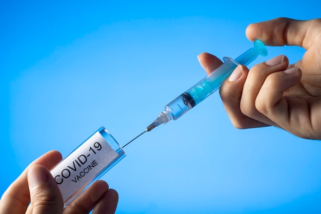 Medico che riempie la siringa con il vaccino contro il coronavirus covid-19. su sfondo blu.