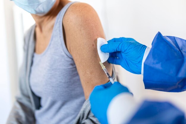 Medico che tiene la siringa che fa la dose di iniezione di vaccinazione covid 19 nella spalla della paziente che indossa la maschera. Concetto di studi clinici sul vaccino influenzale influenzale, trattamento del virus corona, vista ravvicinata.