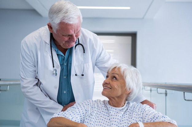 Medico che tiene paziente anziano sulla sedia a rotelle nel passaggio