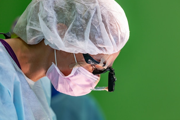 Medico chirurgo femminile che indossa maschera protettiva e cappello durante l'operazione.
