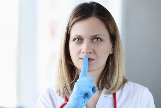 Medico con i guanti che tengono il dito indice vicino alla bocca. Segreto medico concetto