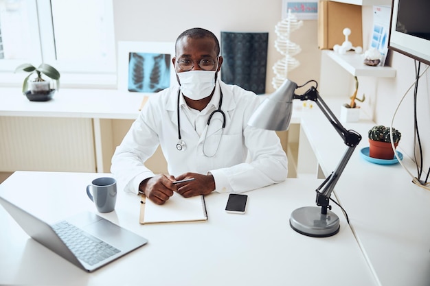 Medico con una maschera che posa per la macchina fotografica alla sua scrivania