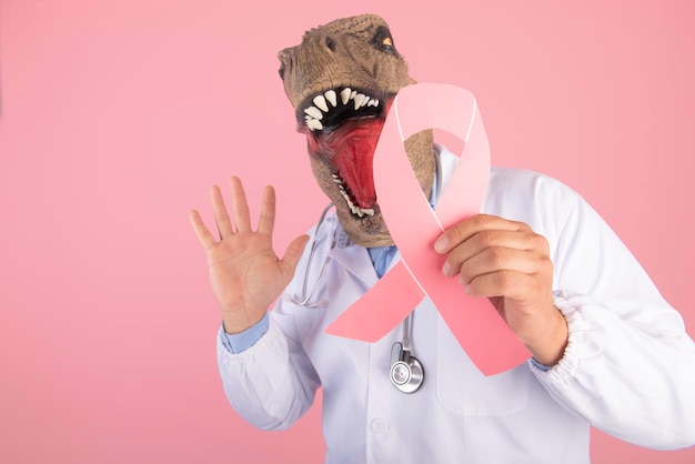 Medico con una testa di dinosauro che tiene il simbolo della lotta contro il cancro da vicino su uno sfondo rosa isolato