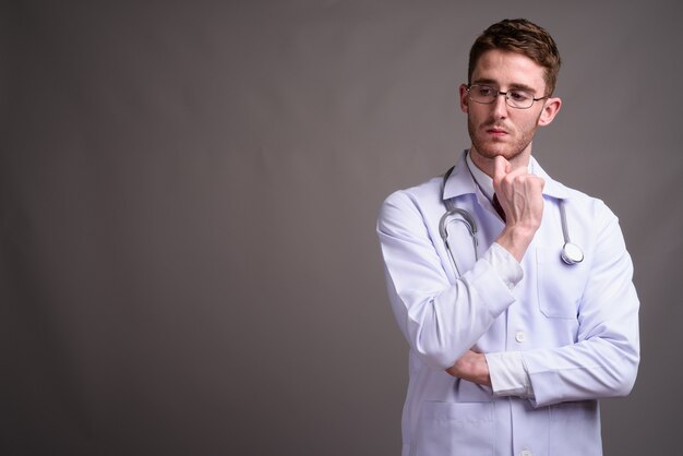 Medico del giovane uomo bello che indossa occhiali da vista contro il grigio