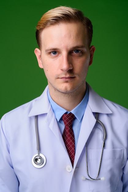 Medico del giovane uomo bello con capelli biondi contro backgrou verde