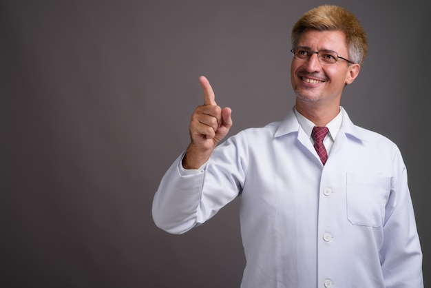 Medico dell'uomo con capelli biondi contro il muro grigio