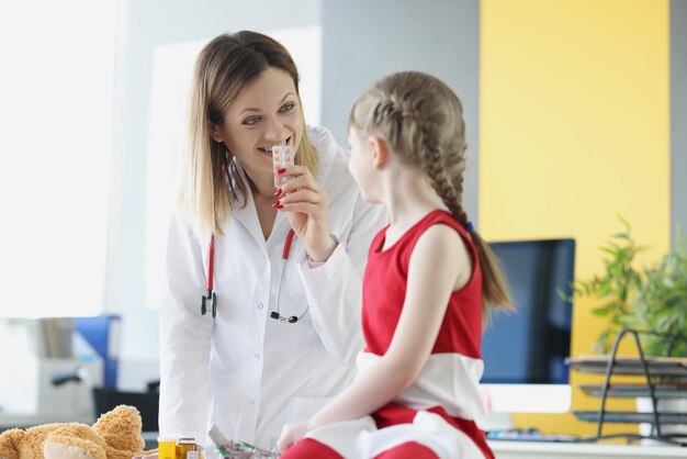 Medico della donna che mostra la bolla della bambina con il farmaco nel trattamento clinico dell'infanzia