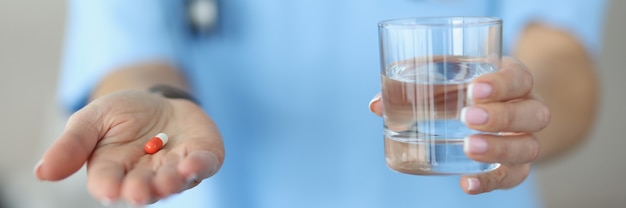 Medico della donna che tiene la capsula della medicina e bicchiere d'acqua nelle mani in primo piano clinica