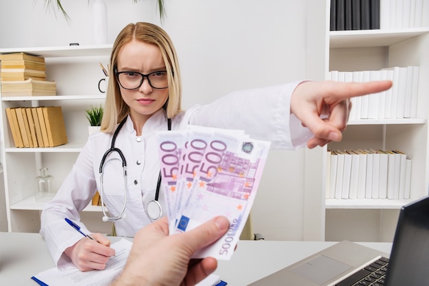 Medico della donna con lo stetoscopio che rifiuta tangenti o tangenti, valute euro, paziente che dà soldi per servizi medici, concetto di corruzione