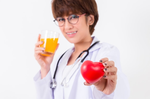 Medico della donna felice che tiene il cuore rosso e succo d&#39;arancia. Isolato su sfondo bianco Studio lig